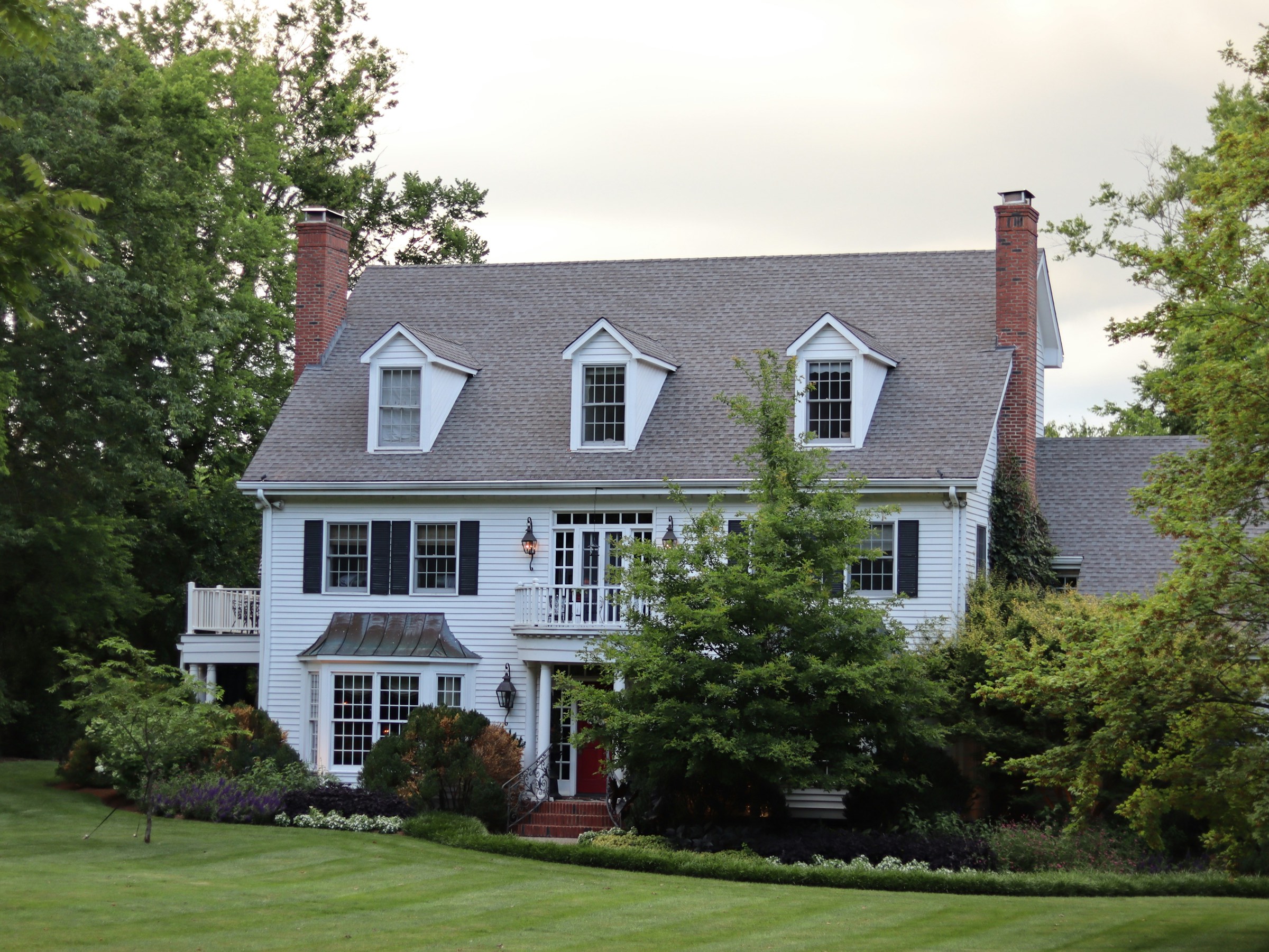 White colonial home with dormers and a landscaped lawn